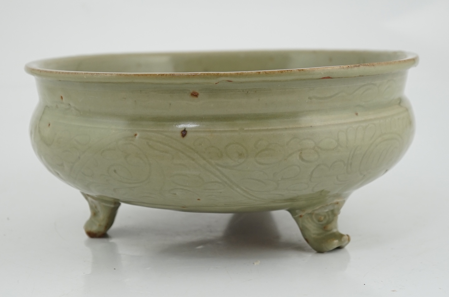 A Chinese Ming Longquan celadon tripod censer, 14th/15th century, the exterior incised with scrolling foliage, on three animal mask feet, burnt orange ring to base, 26.7cm diameter, original receipt for Wing Kei curios,